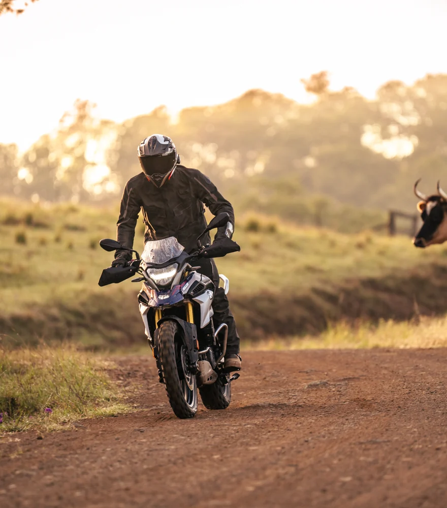 Adventure rider on a dirt road at sunrise through open farmland