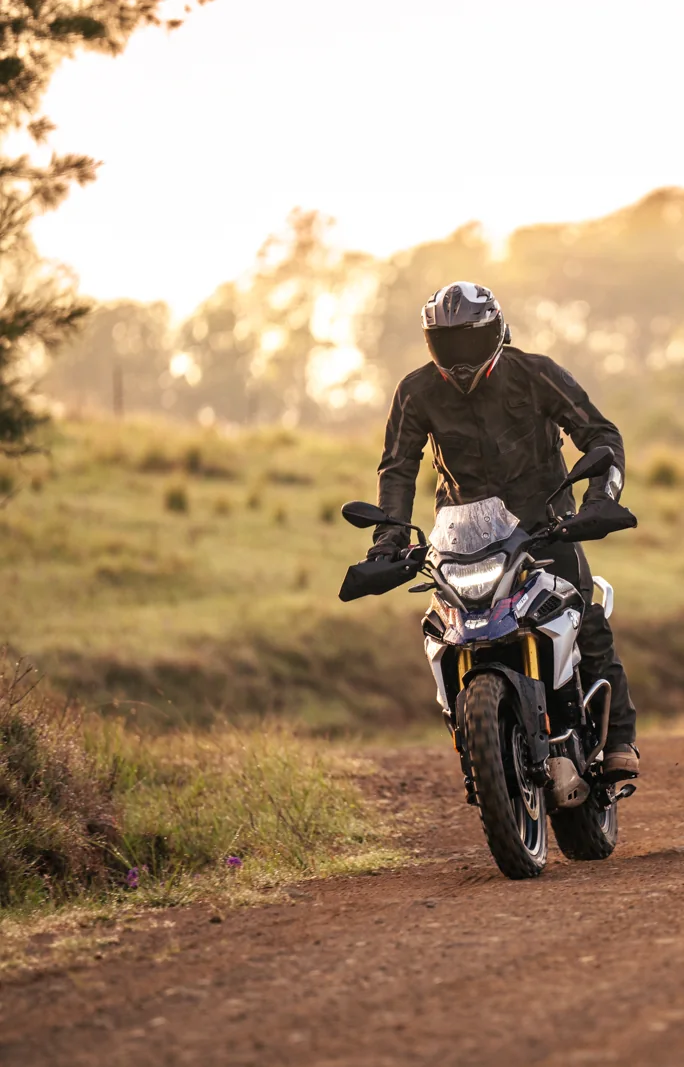 Adventure rider on a dirt road at sunrise through open farmland